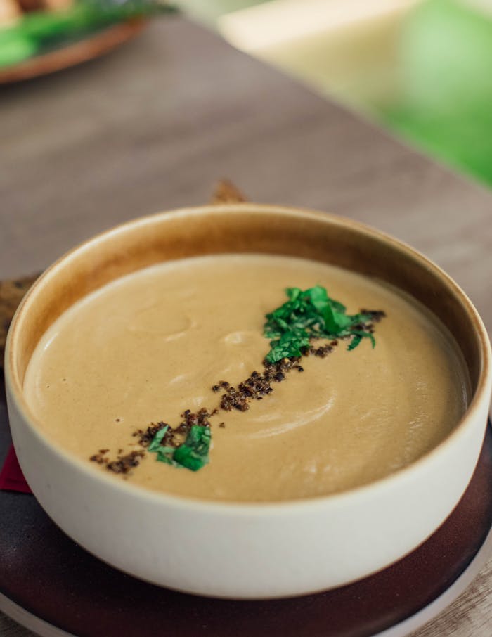 Delicious creamy soup garnished with herbs in a ceramic bowl on a wooden table.